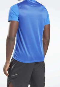 Blå idrottströja med korta ärmar, tillverkad av strukturerad, andningsbar tyg, parat med svarta shorts med prickigt mönster.