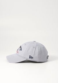 Gorra gris con visera curva, que presenta logotipos bordados en azul marino y rojo. La tela tiene un acabado texturizado y una construcción de seis paneles.