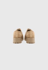 Chaussures en daim tan au bout arrondi, avec une semelle épaisse et crantée, et un design minimaliste. L'arrière présente une finition lisse et des coutures discrètes.
