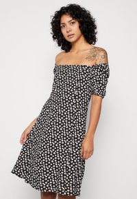 Vestido off-shoulder preto com estampas florais brancas, apresentando mangas bufantes e corpete justo, abrindo na altura do joelho.