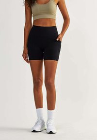 Black athletic shorts with a high waist, featuring side pockets. Paired with a beige crop top and white sneakers with gray accents.