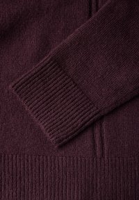 Pull en tricot bordeaux foncé avec des poignets côtelés et un corps texturé. Matière douce, poids moyen, avec une finition lisse.