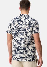 Camisa de manga corta en blanco con un patrón abstracto azul marino, con un cuello tipo solapa y una tela texturizada. La vista posterior muestra un ajuste relajado.