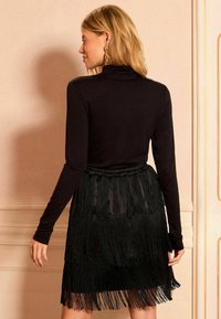 Fekete, hosszú ujjú felső, fekete, rojtos szoknyával párosítva. A szoknya réteges rojtokkal és sima derékpánttal rendelkezik, amely texturált megjelenést kölcsönöz.