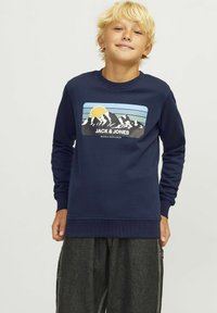 Navy blue sweatshirt featuring a mountain graphic with a yellow sun, text "JACK & JONES" and "WORLD EXPLORER," ribbed cuffs, and hem.