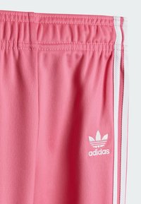 Calças de desporto rosa feitas de um tecido suave, com uma cintura elástica, riscas brancas nas laterais e um pequeno logótipo bordado.