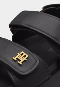 Μαύρο δερμάτινο σανδάλι με χρυσό αναδιπλούμενο λογότυπο TH στη μπροστινή ρυθμιζόμενη κορδέλα, που διαθέτει μαξιλαρωμένο πέλμα και παχιά σόλα.