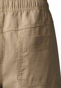 Détail d'un pantalon en lin beige montrant la ceinture élastique et la poche arrière carrée cousue.