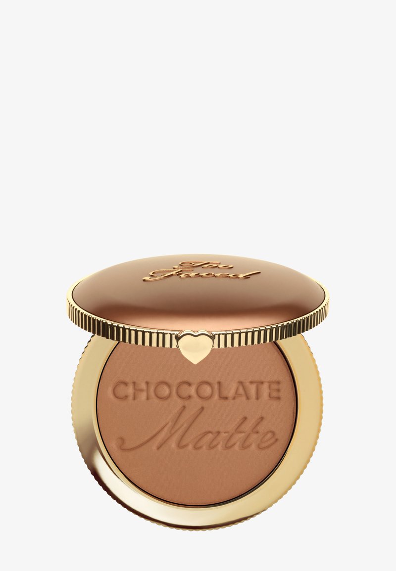 Bronzer compact met een gouden deksel en een hartvormige sluiting. Het poeder is in een matte chocoladeschaduw, met de tekst "Chocolate Matte" erin geperst.