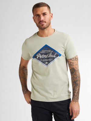 Lys grøn bomulds t-shirt med et blåt og sort diamantgrafiktryk med tekst. Korte ærmer og rund hals. Modellen har sorte shorts på.