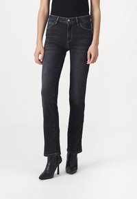 Jeans en denim noir à coupe droite, avec poches avant et coutures contrastées. Portés avec des bottes à talons aiguilles noires.