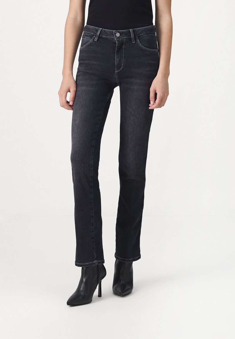 Jeans en denim noir à coupe droite, avec poches avant et coutures contrastées. Portés avec des bottes à talons aiguilles noires.