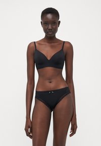 Ensemble de lingerie noire comprenant un bralette triangulaire lisse et un slip assorti avec des bordures en dentelle et un petit nœud décoratif à la taille.