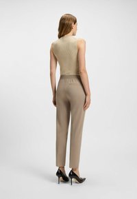 Beige geribbelde mouwloze top, gecombineerd met op maat gemaakte beige broek met achterzak; model draagt zwarte hoge hakken.