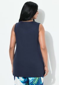 Marinblå ärmlös topp med avslappnad passform, med rund halsringning och slät textur, tillsammans med mönstrade blommiga byxor.