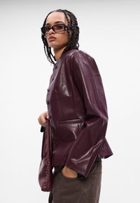 Burgundská kožená bunda s lesklým povrchom, s mandarínkovým golierom, zipsom a dvoma bočnými vreckami.