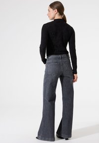 Haut noir à manches longues avec un motif floral texturé, associé à un jean large gris. Le jean est doté d'un design à cinq poches et de détails de couture.