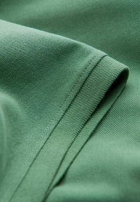 Tissu de coton vert avec une texture lisse, montrant des bords repliés et des coutures. Le matériau est léger et légèrement extensible.