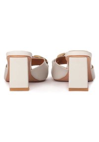 Chaussures à talon bloc blanc cassé avec une tige lisse, un dos ouvert arrondi et un talon rectangulaire. Présente un accent doré sur la sangle.