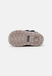 Des chaussures bleues avec une semelle en caoutchouc texturée, présentant un motif de grip solide et un détail de logo. Conçues pour la durabilité et l'adhérence.