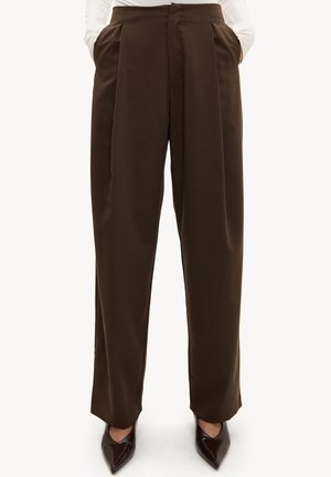 Pantalon large taille haute de couleur brun foncé, porté avec une chemise blanche rentrée et des chaussures pointues brun foncé.