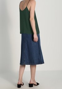 Grön ärmlös topp med tunna axelband, ihop med en knälång A-linjeformad denimkjol. Bärs med svarta klacksandaler.