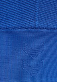 Zbliżenie niebieskiego teksturowanego materiału z dwoma wzorami w kształcie szewronów skierowanych w dół, dzierganych w tkaninie.