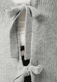 Gray knitted cardigan featuring a textured pattern, with two bows at the front and a soft, fuzzy fabric. Notable for its open design.