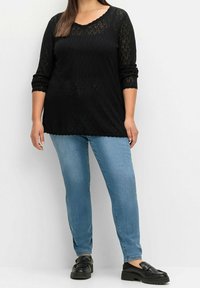 Černý pletený top s výstřihem do půlkruhu a rukávy tři čtvrtě, doplněný světlými modrými džíny a černými plochými botami s texturovaným povrchem.