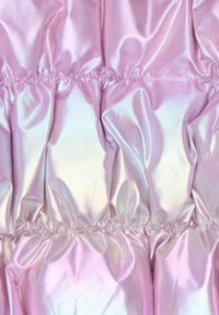 Iridescent rosa puffy tyg som har samlade sektioner med en slät, glänsande yta och en sträckt söm, som reflekterar ljus på olika sätt.