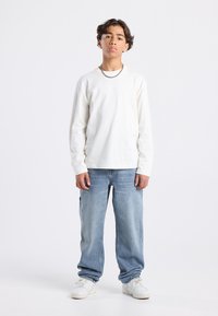 Long-sleeve white cotton T-shirt paired with light blue relaxed-fit jeans, and white athletic sneakers. Simple design, casual style.