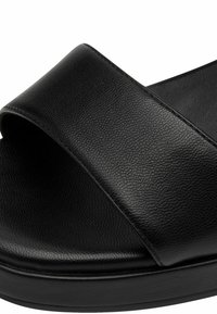 Musta liukusandaali, jossa on sileä tekstiilistrap ja pehmeä pohja, sekä pyöristetyt reunat. Minimalistinen muotoilu ilman näkyvää metalliosaa.
