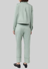 Zestaw składający się z miętowozielonej kurtki i spodni wykonany z lekkiego materiału, z kurteczką o kroju cropped, z plisą z tyłu i spodniami z wywiniętymi nogawkami, zestawiony z czarnymi butami.