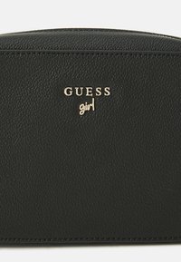Schwarze strukturierte Kunstledertasche mit goldfarbenem "GUESS"-Logo und kleinerem "girl"-Text. Verfügt über eine glatte Oberseite und gestickte Ränder.