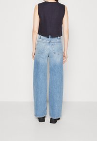 Marineblaue ärmellose Bluse mit einem Rückenschlitz, kombiniert mit hellblauen, hoch taillierten weit geschnittenen Jeans mit zwei Gesäßtaschen und einer verwaschenen Optik.