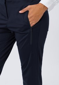 Marineblauwe stretchbroek met een slim fit, voorzien van een ritszak aan de zijkant en een gladde, gestructureerde stofafwerking.