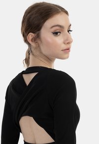 Svart ribbat långärmat topp med twist-back-design, som har en öppen rygg och en mjuk textur.