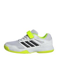Scarpe sportive bianche con strisce nere, dettagli verdi, materiale in rete, suola in gomma e una fascia in Velcro. Texture notevole sulla parte superiore.