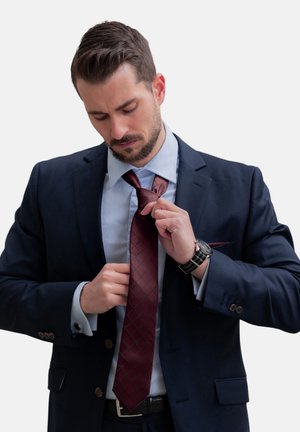 Cravate bourgogne avec un motif en losanges portée avec un costume noir. Chemise bleu clair sous la veste, montre en argent au poignet.