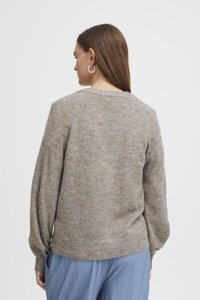 Maglione lavorato a maglia in beige chiaro con una finitura textured. Presenta un collo a giro, maniche raglan e orlo a costine, abbinato a pantaloni blu larghi.