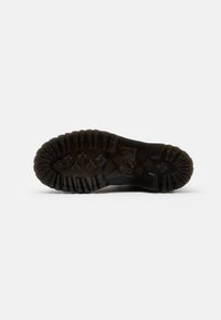 Semelle d'une botte noire avec des crampons profonds, des motifs rectangulaires et en forme de losange, et un texte en relief sur la zone de la voûte.