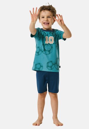 Teal T-shirt met een patroon van voetballen en "10" in beige, gecombineerd met marineblauwe shorts. Korte mouwen, zachte stof en een relaxte pasvorm.