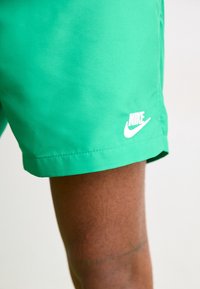Gröna Nike-shorts med en mjuk yta, med en vit logotyp på den nedre fållen. Designen inkluderar en enkel, avslappnad passform.