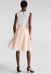 Lichtroze, knielange rok met een zachte, vloeiende textuur, gecombineerd met een witte mouwloze top met een keyhole-detail op de rug.