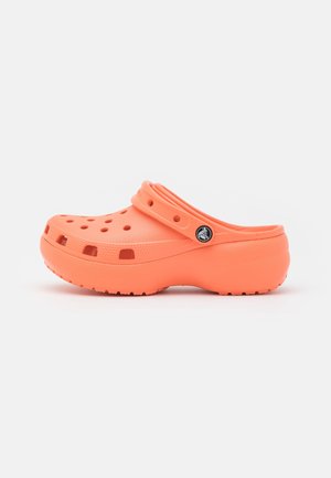 Zueco naranja sin cordones con orificios de ventilación, correa ajustable en el talón y suela texturizada, mostrado de lado sobre un fondo liso.