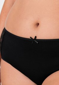 Slip in cotone nero con una texture liscia, dotato di un piccolo fiocco nero e dettagli in pizzo sui lati.