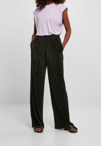 Světle fialový top bez rukávů v kombinaci s tmavě zelenými širokými kalhotami s žebrováním, které mají elastický pas a boční kapsy. Černé ploché sandály.