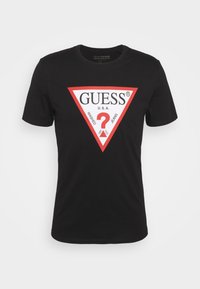 Camiseta negra de algodón, con un gran logo triangular blanco con acentos rojos, que muestra "GUESS U.S.A." y un signo de interrogación.