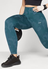 Teal hoge taille legging met een subtiel camouflagepatroon en gestikte details. Zwart sport schoenen met een mesh textuur en veters.