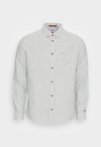 Camisa de botones de manga larga a rayas verdes y blancas, hecha de algodón, con un bolsillo en el pecho y una etiqueta de marca en la manga.